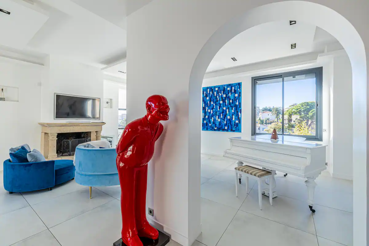 Salon d'une villa luxueuse aux murs blancs. Il y a un piano , une cheminée et deux canapés.