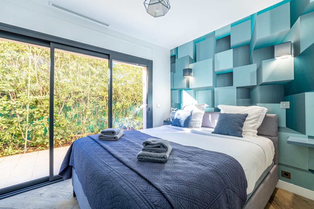 Une chambre de la Villa Jaliel aux tons bleu ciel. Il y a une baie vitrée avec vue sur un environnement verdoyant.